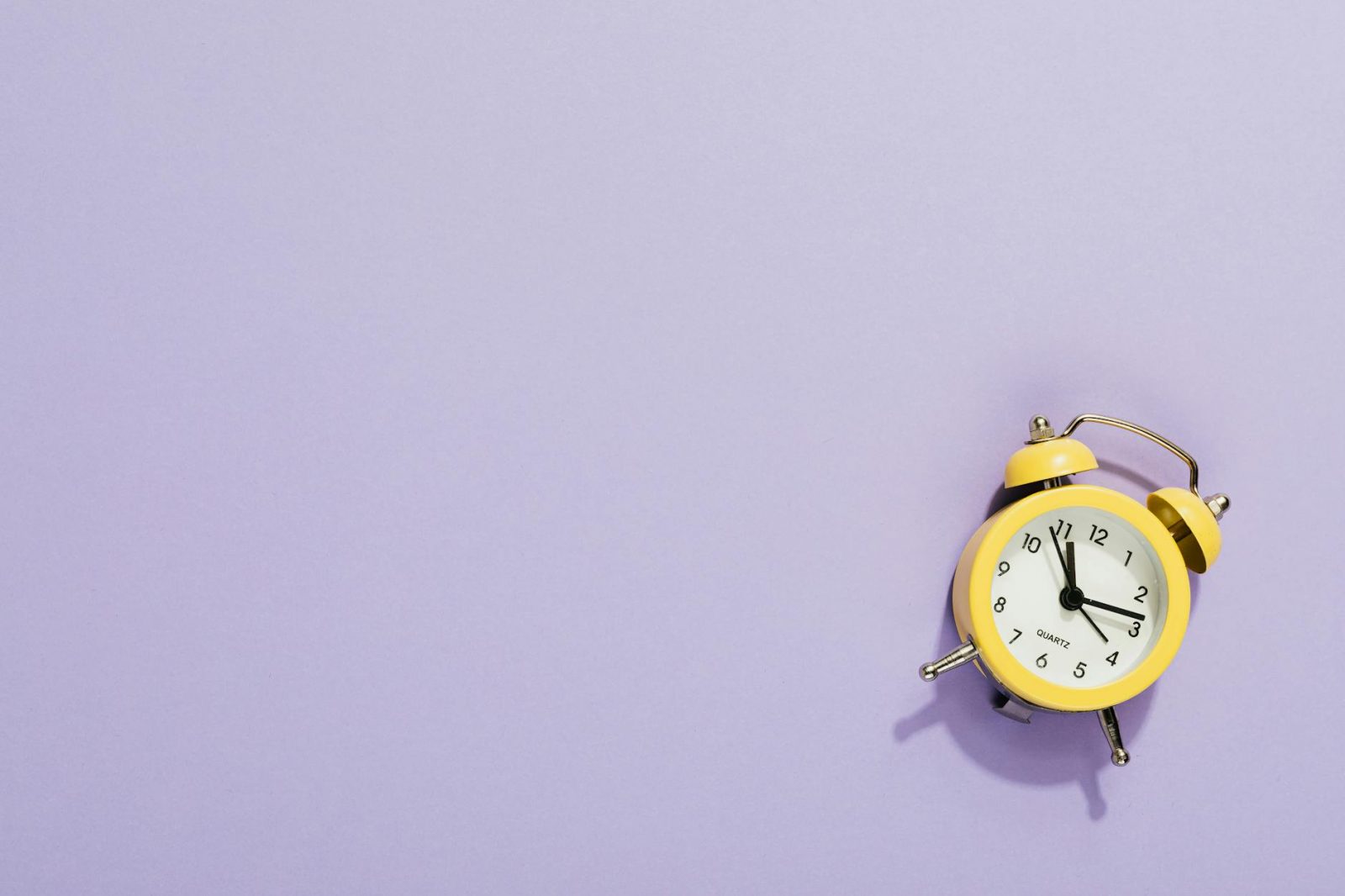 close up shot of a yellow alarm clock on a purple surface